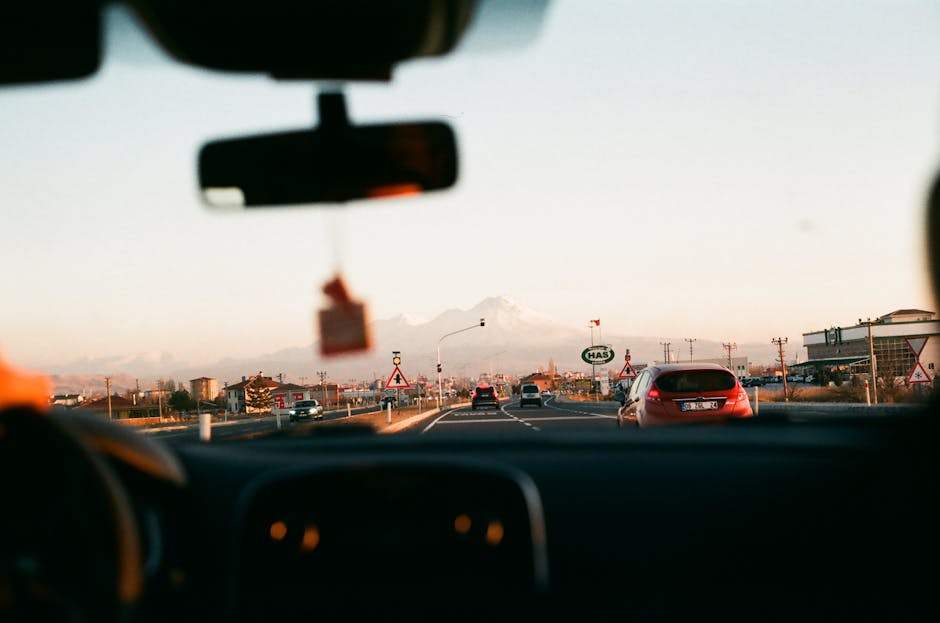 View from inside a car driving towards a mountainous landscape during sunset with beautiful sky.
