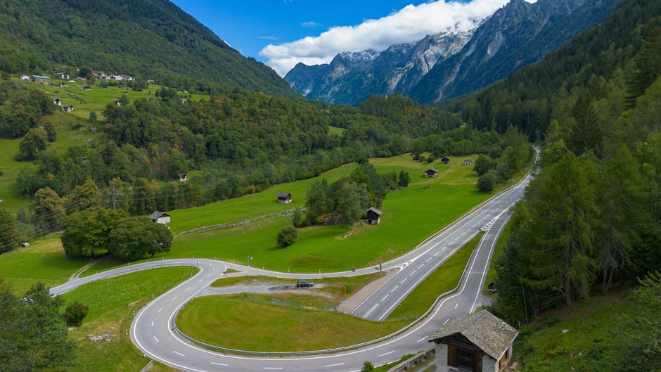 A winding road cuts through the lush green valley of Bregaglia, Switzerland with mountain views.