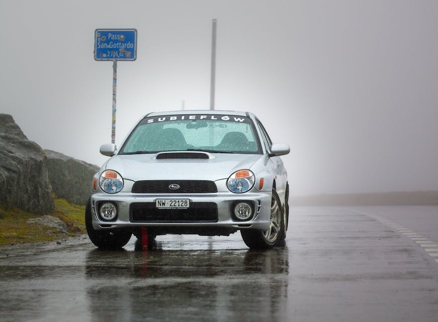 Silver car parked at rainy San Gottardo pass with foggy atmosphere.